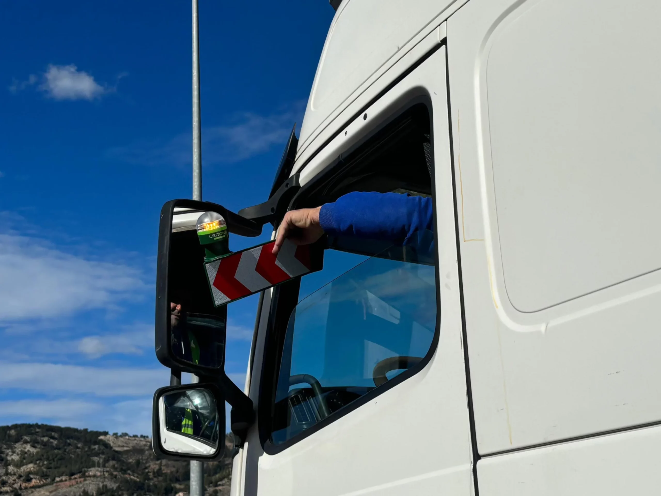 conductor colocando la baliza v16 conectada de ledone para camiones
